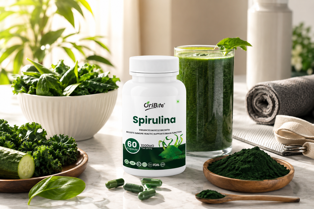 "A white bottle of Oribite Spirulina Capsules on a kitchen counter next to a tall glass of green smoothie, a bowl of dark green spirulina powder, and fresh green vegetables like cucumber and kale."
