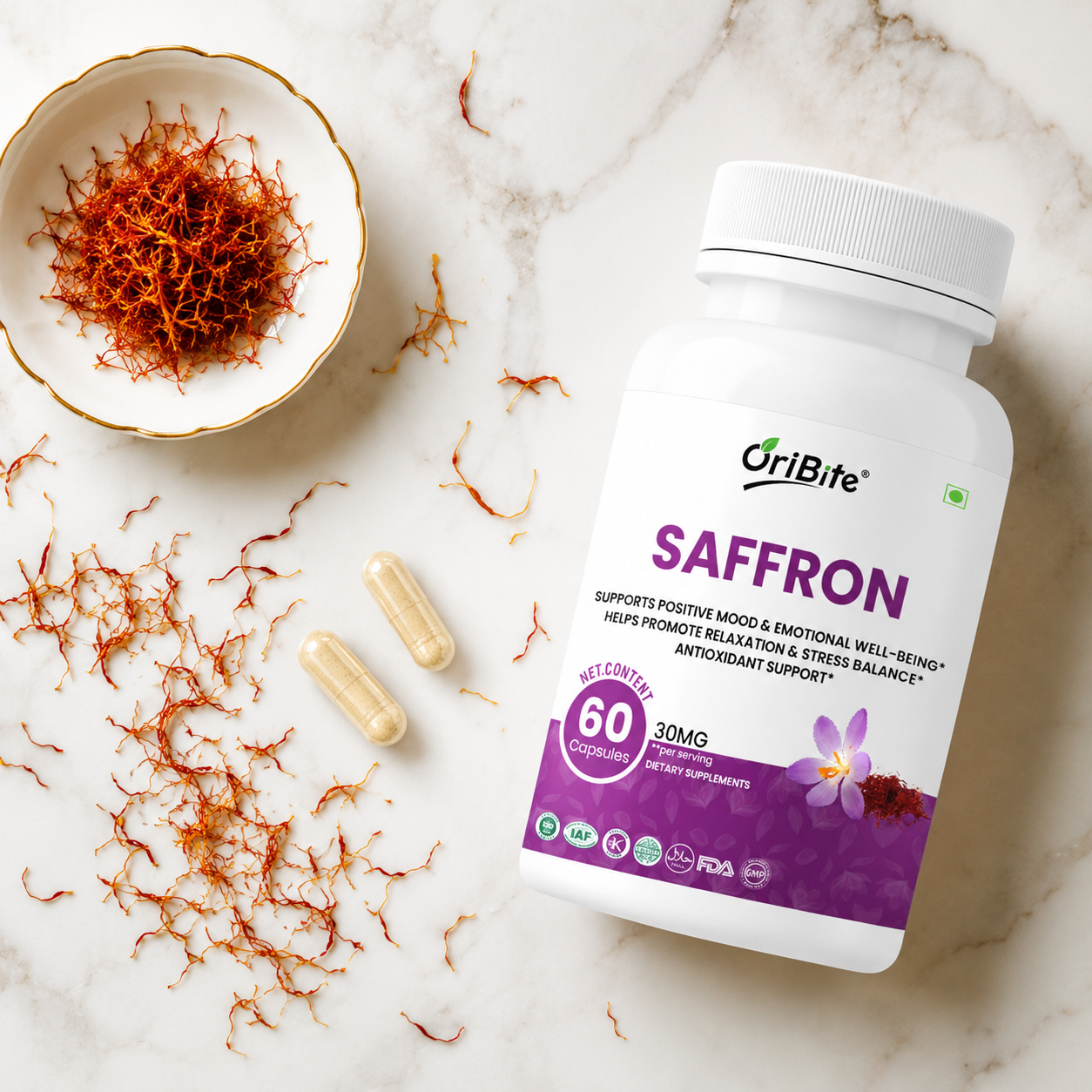 A white bottle of Oribite Saffron capsules next to two loose yellow capsules and loose dried saffron strands on a light textured surface.